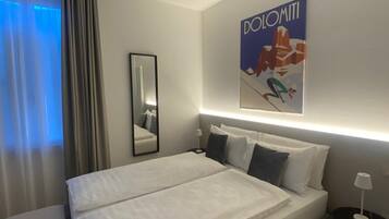 A modern hotel room with a large bed, a bedside table with a lamp, a mirror, and a wall-mounted artwork.