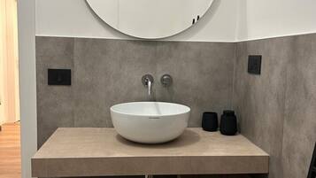 Ein modernes Badezimmer mit einem runden Spiegel, einem weißen Waschbecken und einer Holzschatulle mit dem Aufdruck "ENDRIZZI".