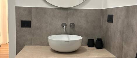 A modern bathroom with a round mirror, a white sink, and a wooden box labeled "ENDRIZZI".