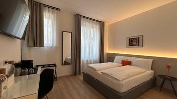 A hotel room with a bed, a desk, a chair, a TV, and a bedside table.