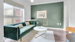 A modern living room with a green sofa, a round coffee table, and a framed picture on the wall. - 1-Bedroom City Sophistication: Unwind in Style! (London)