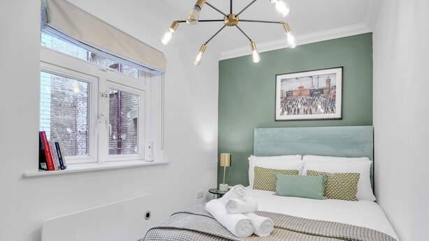 Une chambre à coucher avec un lit, une fenêtre, un tableau accroché au mur et une table de chevet avec une lampe.
