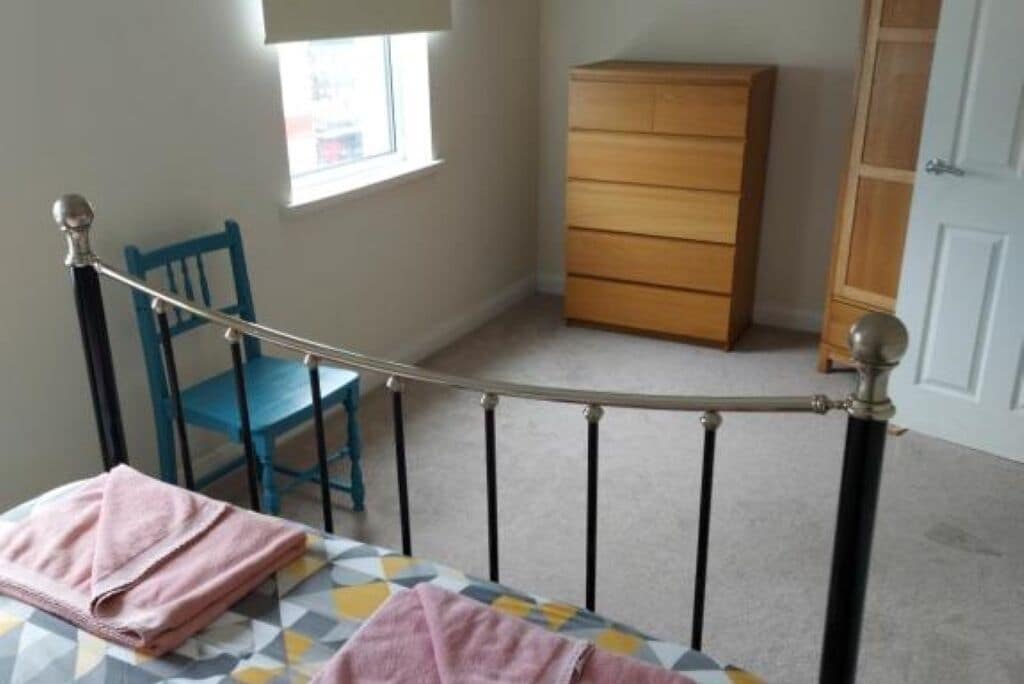 Une chambre à coucher avec un lit, une commode en bois, une chaise et une fenêtre.