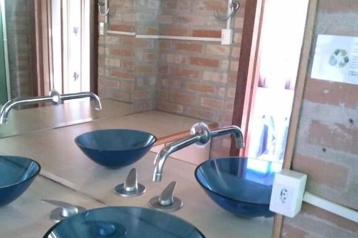 A bathroom with three blue glass sinks, a mirror, and a brick wall.