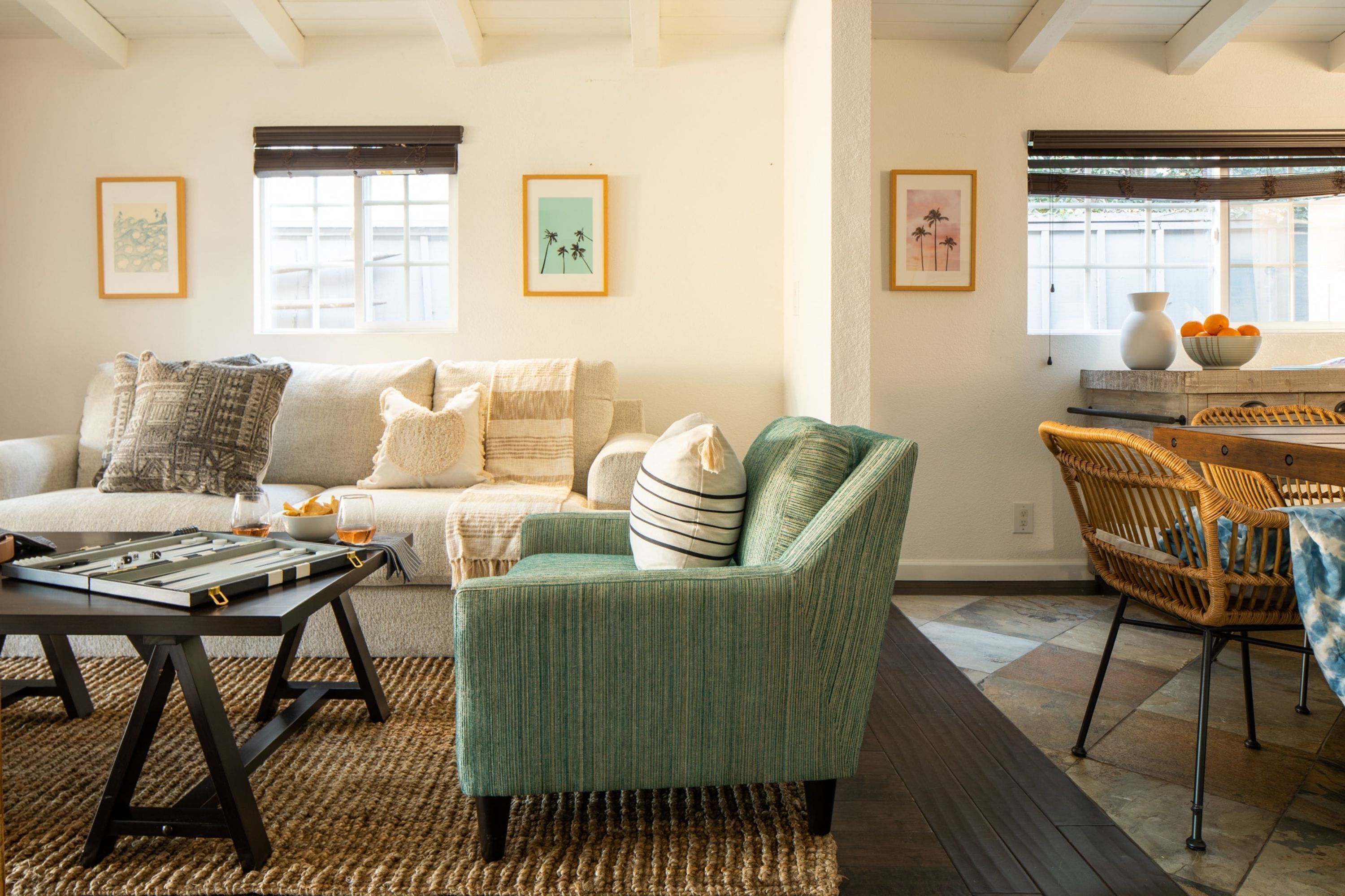 A cozy living room with a sofa, armchair, and a coffee table. There are framed pictures on the walls and a window with a view.