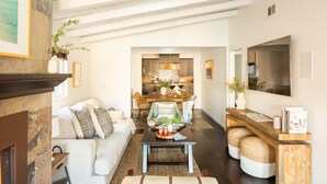A modern living room with a fireplace, a dining area with a wooden table and chairs, and a kitchen in the background. - Sand Castle by Avantstay Beach House on Balboa Peninsula w Patio Hot Tub (Newport Beach)