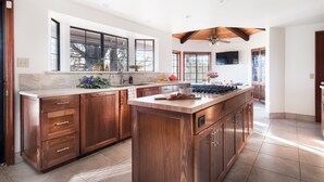 A spacious kitchen with wooden cabinets, a large island, and a window overlooking a tree. - Cathedral by Avantstay Charming Secluded Estate w Sauna Pool Table Views of the Rolling Hills (Templeton)