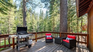 A deck with a grill, wicker furniture, and a view of a forest.