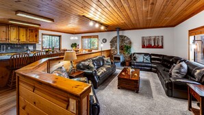 A spacious living area with a large black leather sofa, wooden coffee table, and a wooden bench. A stone fireplace and a stone wall with a circular window are visible.