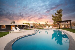 A modern outdoor pool area with lounge chairs, a pergola with string lights, and a sunset view. - Jackrabbit Ridge by Avantstay Entertainers Paradise w Pool Games (Twentynine Palms)