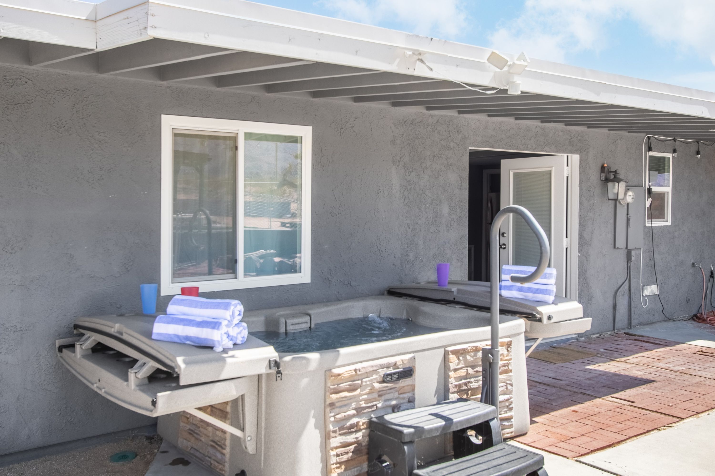 An outdoor hot tub with a stone facade, a window, and a patio area.