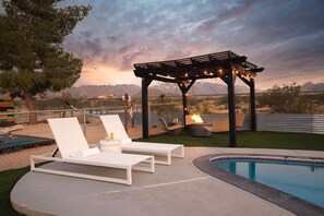 A poolside area with lounge chairs, a pergola with string lights, and a fire pit. - Jackrabbit Ridge by Avantstay Entertainers Paradise w Pool Games (Twentynine Palms)