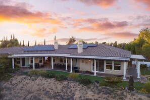 Une maison avec un toit en tuiles, des panneaux solaires et un patio couvert aménagé avec du mobilier d’extérieur.