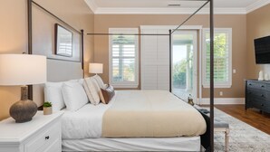 Un dormitorio con cama con dosel, una mesita de noche con lámpara, un aparador y un televisor sobre un mueble.