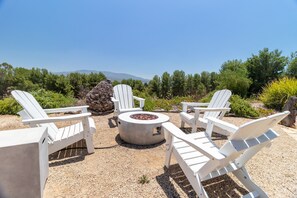 Une terrasse avec quatre chaises Adirondack blanches disposées en cercle autour d’un foyer extérieur.