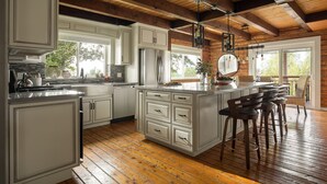 A modern kitchen with white cabinetry, a large island with bar stools, wooden flooring, and a vaulted ceiling.