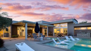Ett modernt hus med en swimmingpool, solstolar och en uteplats.