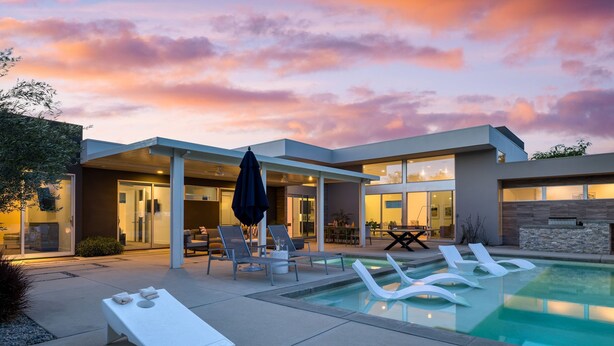 Una casa moderna con piscina, sedie a sdraio e una zona patio.