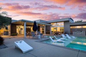 A modern house with a swimming pool, lounge chairs, and a patio area.