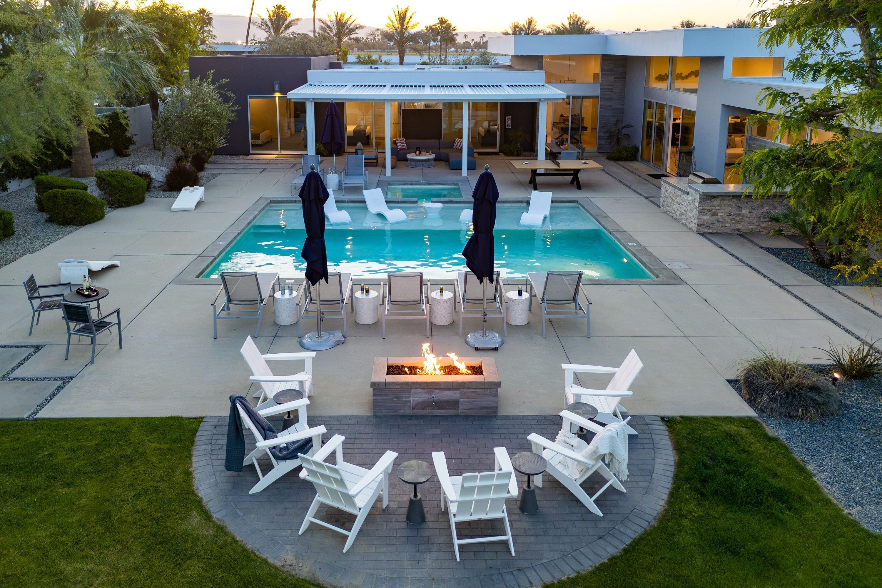 A modern outdoor pool area with lounge chairs, a fire pit, and a covered seating area.