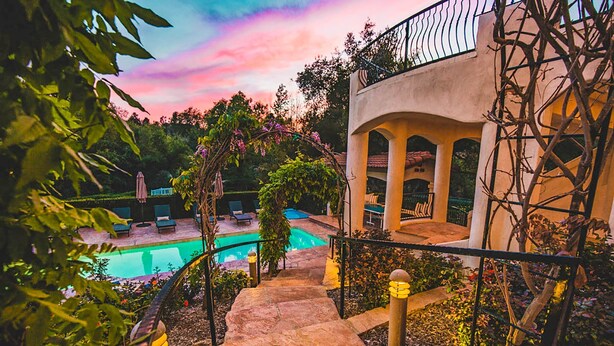 A stone pathway leading to a pool area with a view of a building with arches and a balcony. - De Luz by Avantstay 5 Acre Estate w Lake Pool Hot Tub (Temecula)