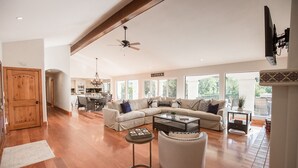 A spacious living room with a large sectional sofa, a coffee table, and a fireplace. There is a dining area in the background with a chandelier. - De Luz by Avantstay 5 Acre Estate w Lake Pool Hot Tub (Temecula)