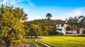 A white building with a red roof, surrounded by a well-maintained garden and a curved pathway. - De Luz by Avantstay 5 Acre Estate w Lake Pool Hot Tub (Temecula)