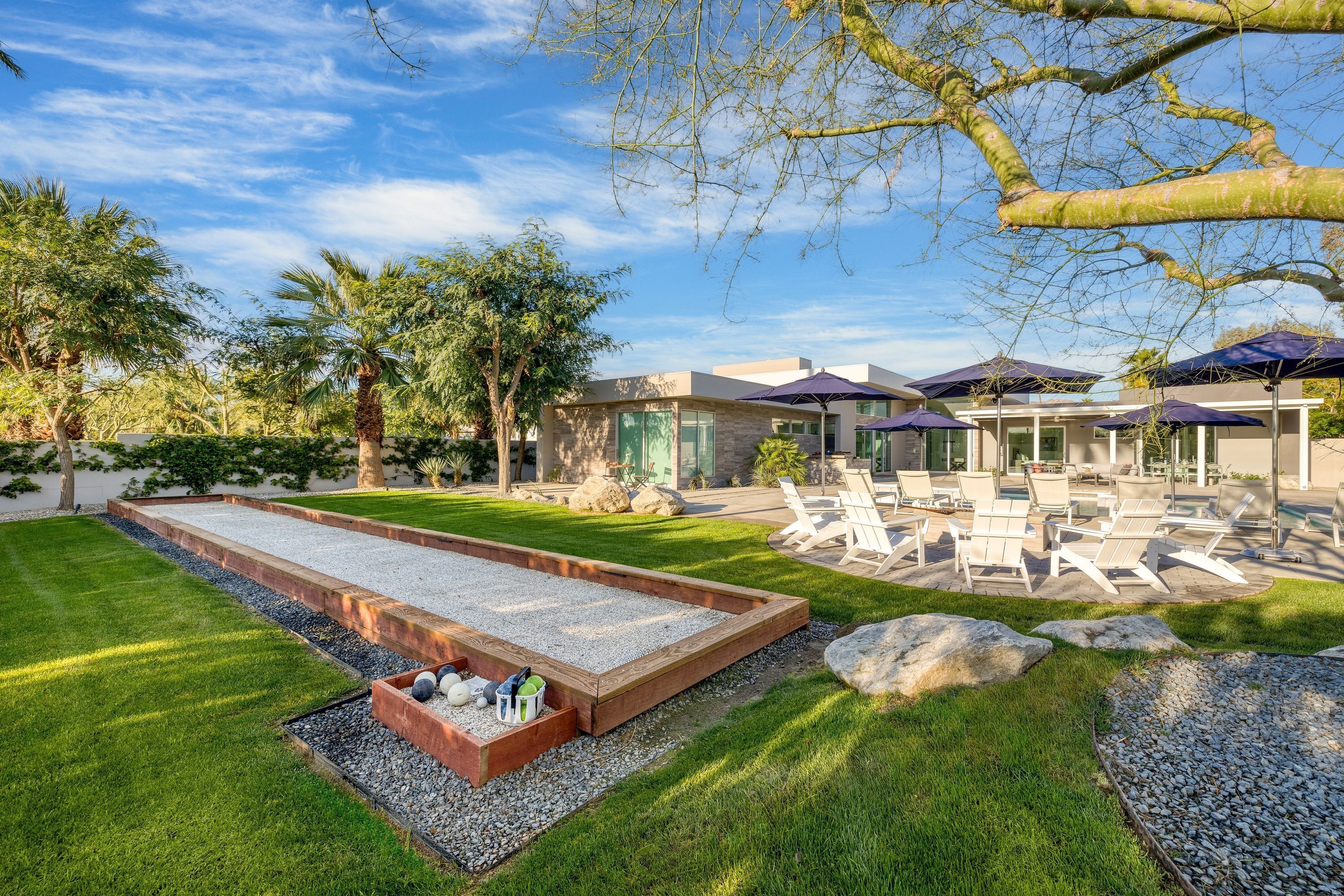 Een verzorgde achtertuin met een putting green, een terras en een modern gebouw met grote ramen.
