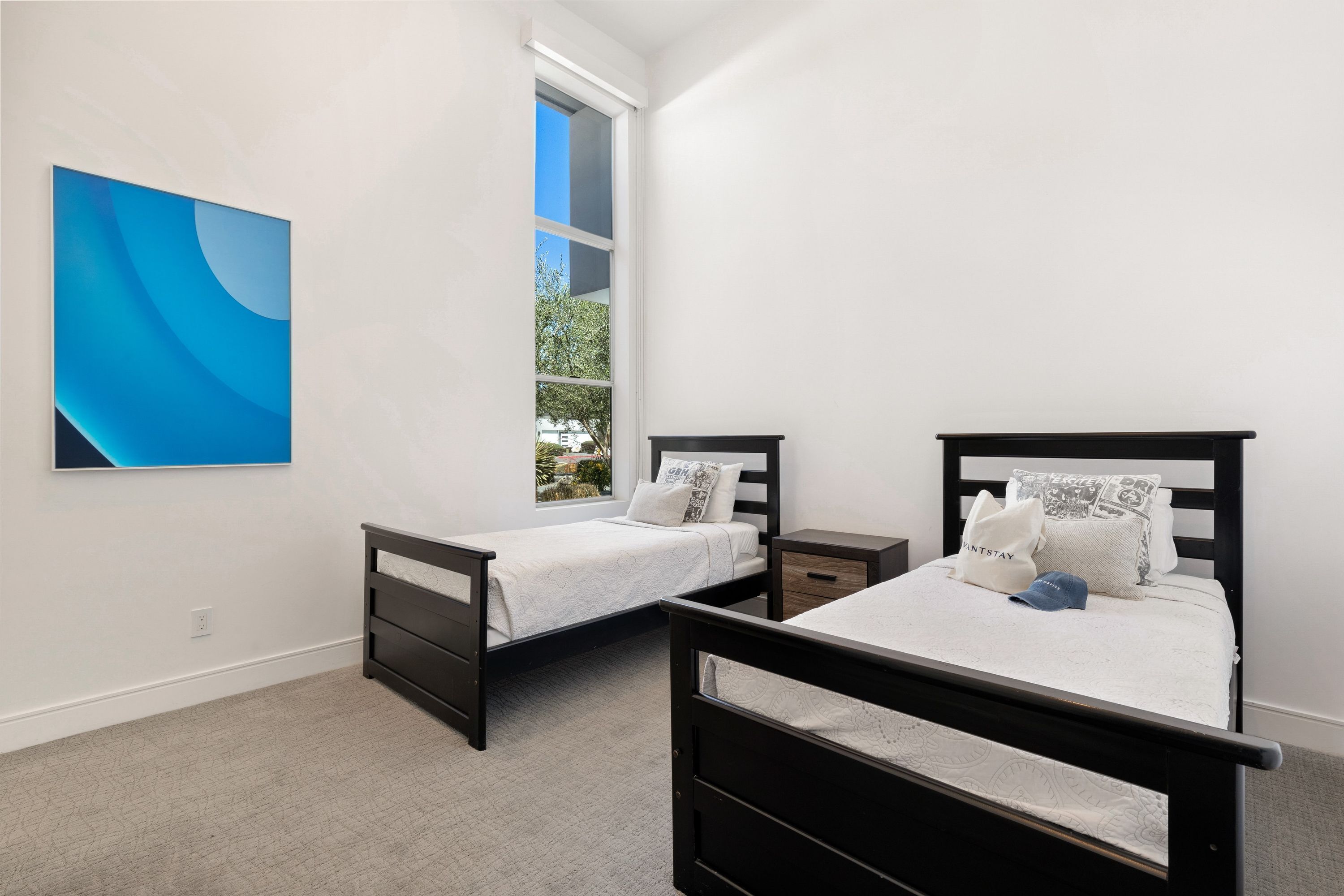 A bedroom with two beds, a large window, and a wall-mounted artwork.
