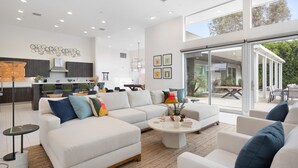 A spacious living area with a large sofa, a coffee table, and a dining area visible through glass doors. - Polo Villa 7 by Avantstay Features Entertainer s Backyard Game Room 260316 5 Bedrooms (La Quinta)