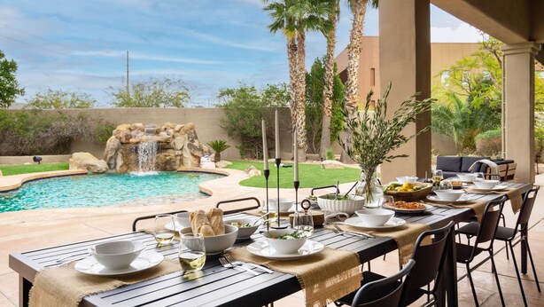 An outdoor dining area with a pool and waterfall backdrop. - Arcadia by Avantstay Breathtaking Oasis in Scottsdale w Pool Hot Tub Game Room (Scottsdale)