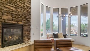 A cozy living room with a stone fireplace, leather chairs, a large window with a view, and a chandelier. - Arcadia by Avantstay Breathtaking Oasis in Scottsdale w Pool Hot Tub Game Room (Scottsdale)