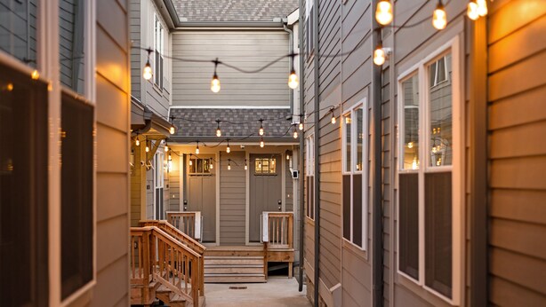 A narrow, covered outdoor corridor with wooden steps leading to a front door, string lights overhead, and a view of the house's exterior. - Hart Suite 13 by Avantstay Gorgeous Town House w Modern Amenities in Nashville (Nashville)