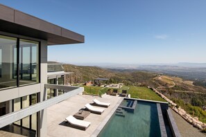 A modern outdoor pool area with lounge chairs, a view of the countryside, and a building with large windows. - Belleza by Avantstay Hilltop Mansion w Pool Panoramic Views Ultra Modern Interior (Glen Ellen)