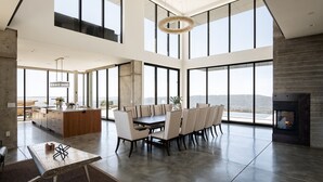 A spacious living area with a large dining table, high ceilings, and large windows offering a view of the outdoors. - Belleza by Avantstay Hilltop Mansion w Pool Panoramic Views Ultra Modern Interior (Glen Ellen)