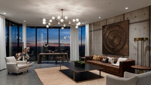 A modern living room with a large window, a chandelier, a leather sofa, and a dining area. - Belleza by Avantstay Hilltop Mansion w Pool Panoramic Views Ultra Modern Interior (Glen Ellen)