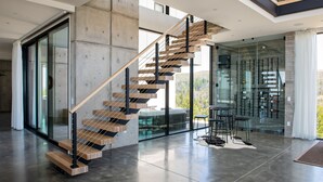 A modern staircase with glass railings and wooden steps, leading to a balcony with a view of the outdoors. - Belleza by Avantstay Hilltop Mansion w Pool Panoramic Views Ultra Modern Interior (Glen Ellen)