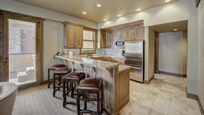 A kitchen with a central island, wooden cabinets, a stainless steel refrigerator, and a window with blinds.