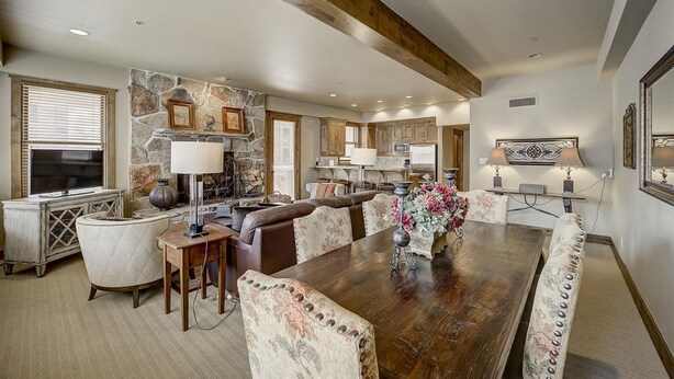 A spacious living room with a large wooden dining table, comfortable seating, a stone accent wall, and a fireplace.