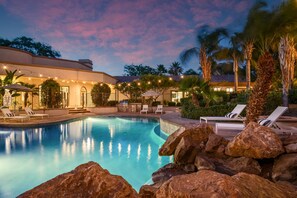 A swimming pool with lounge chairs, surrounded by rocks and palm trees, under a twilight sky. - Villa Verbena by Avantstay Expansive Estate w B-ball Court Pool Spa Entertainer s Yard (Indio)