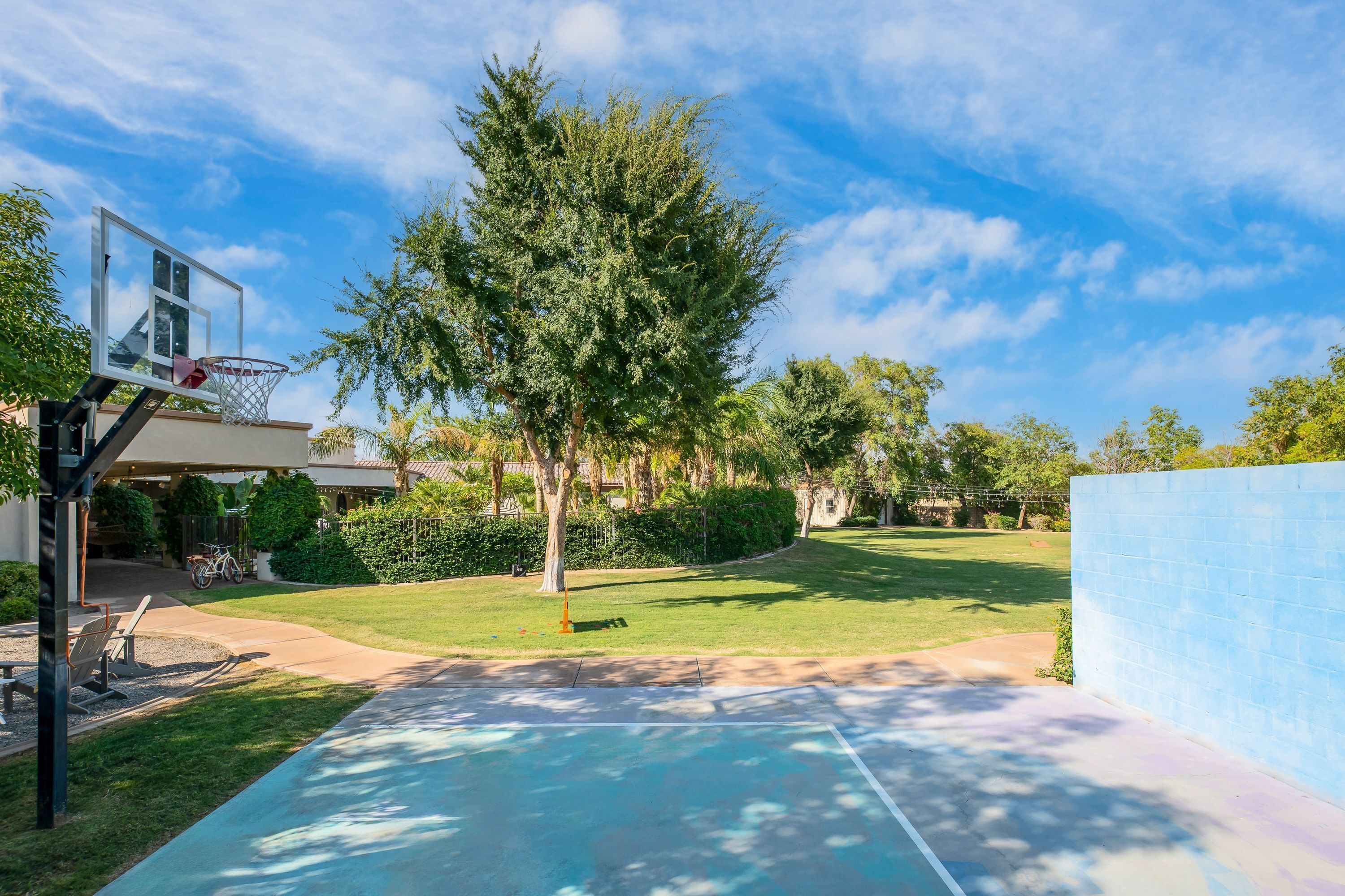 An outdoor basketball court with a hoop, surrounded by a well-maintained lawn and trees.
