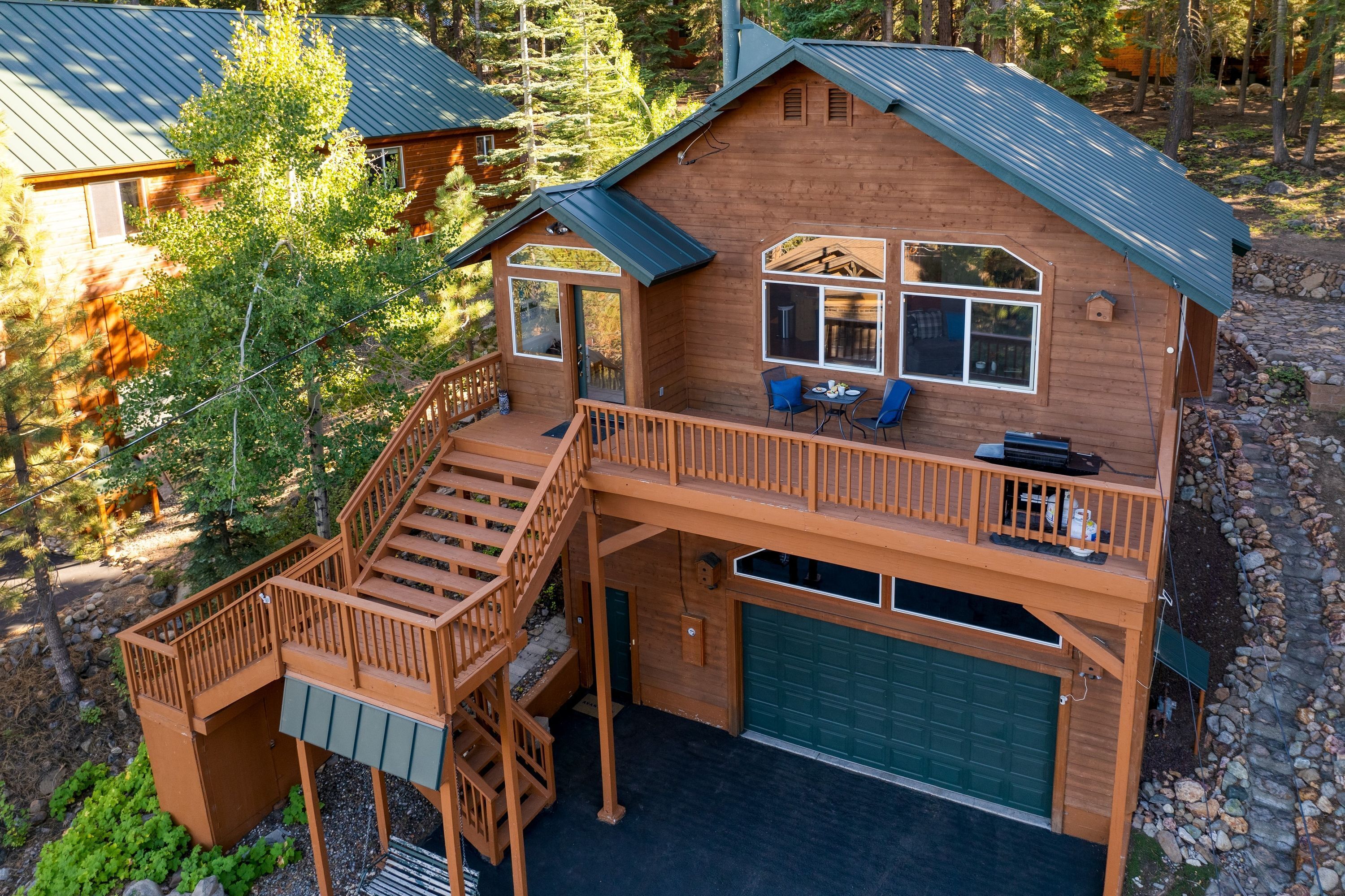 A two-story wooden cabin with a balcony, a garage, and a deck.