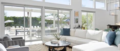 A spacious living room with a white sofa, a round coffee table, and a large glass door leading to an outdoor patio area.
