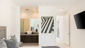 A modern bedroom with a large bed, a flat-screen TV mounted on the wall, and a view into the bathroom. - Polo Villa 2 by Avantstay Entertainer s Backyard w Pickleball Court Pool Spa 260314 6 Bedrooms (La Quinta)
