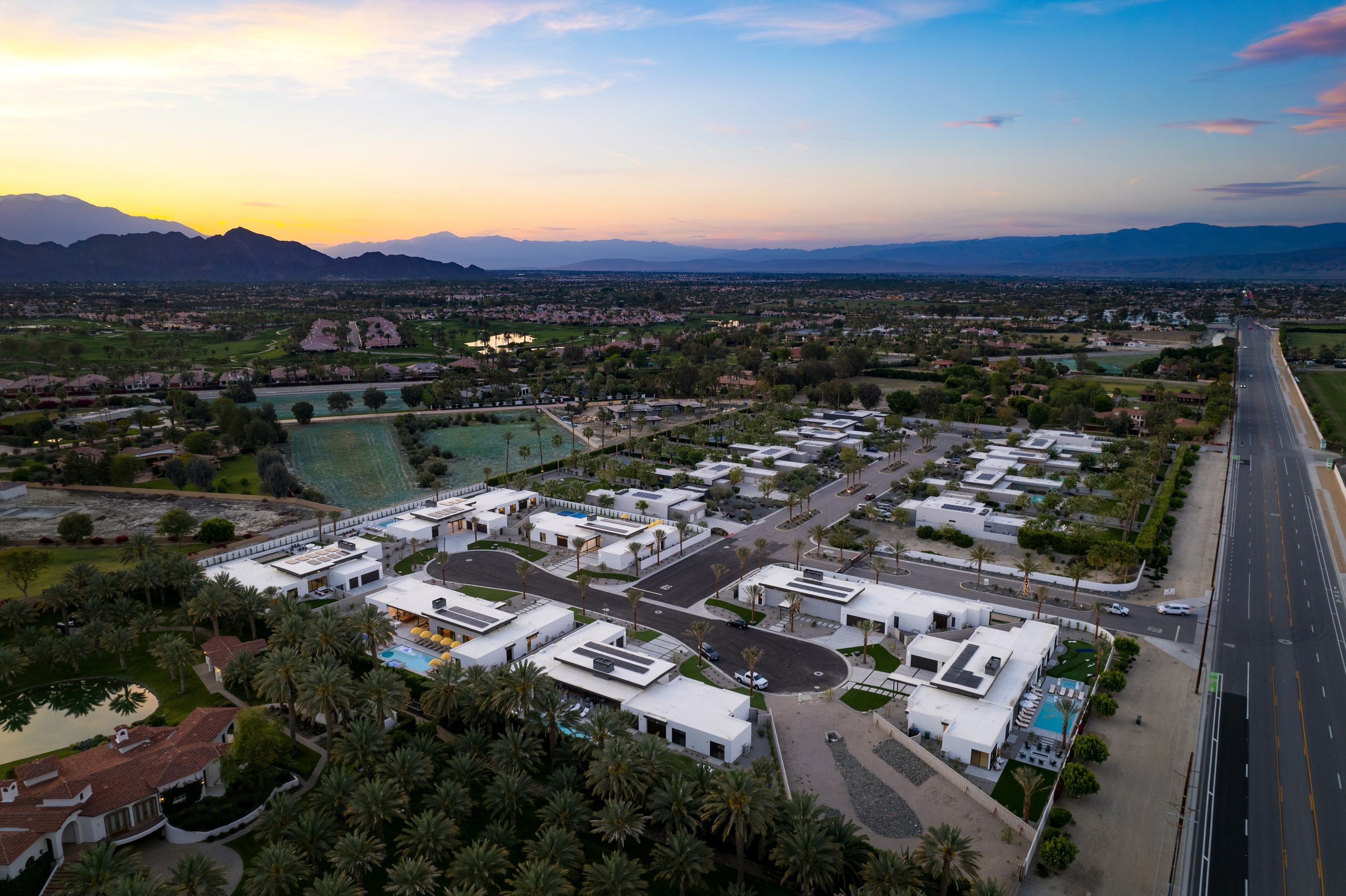 An aerial view of a residential area with modern houses, a road, and a highway in the background.