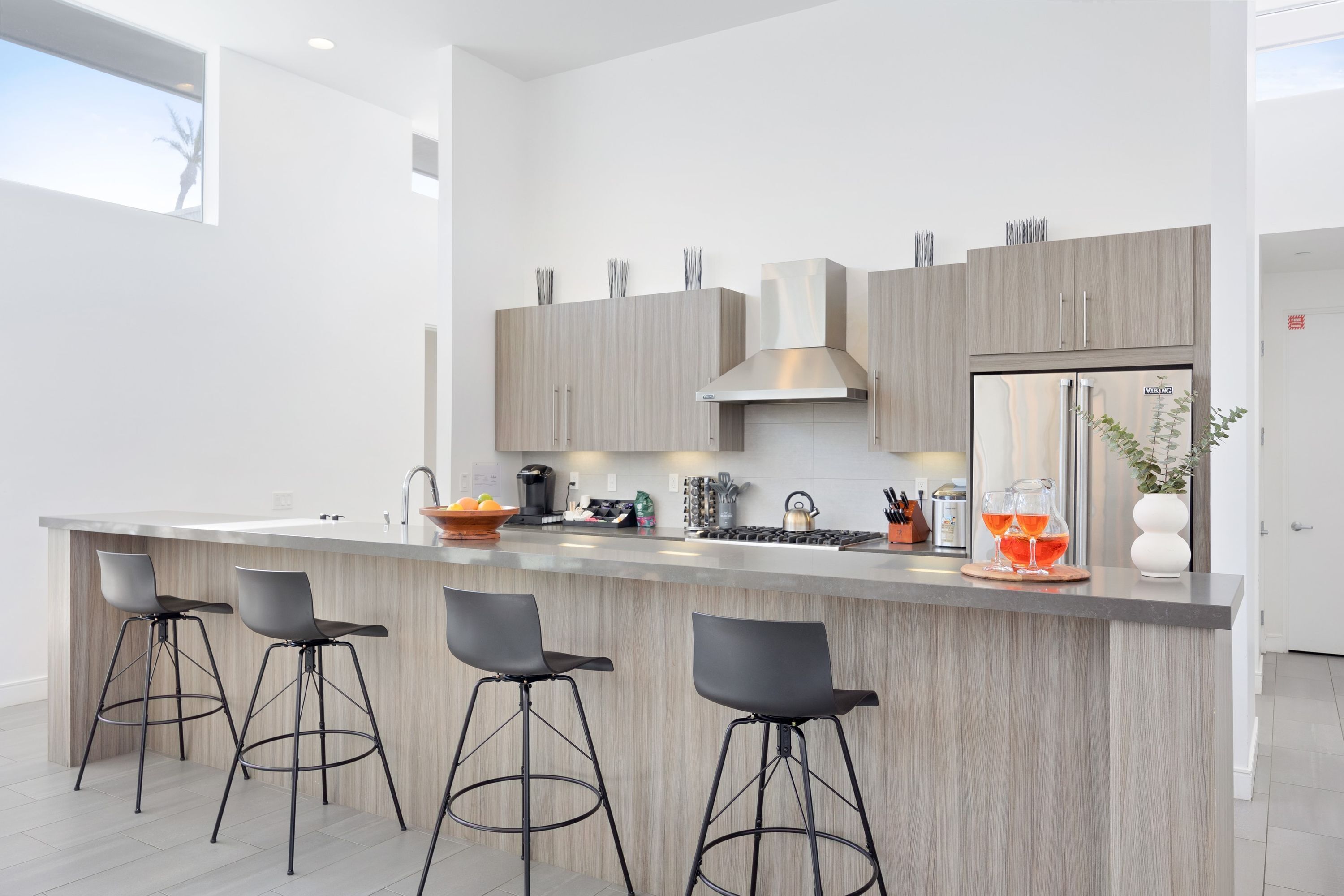 A modern kitchen with a central island, bar stools, and a stainless steel refrigerator.
