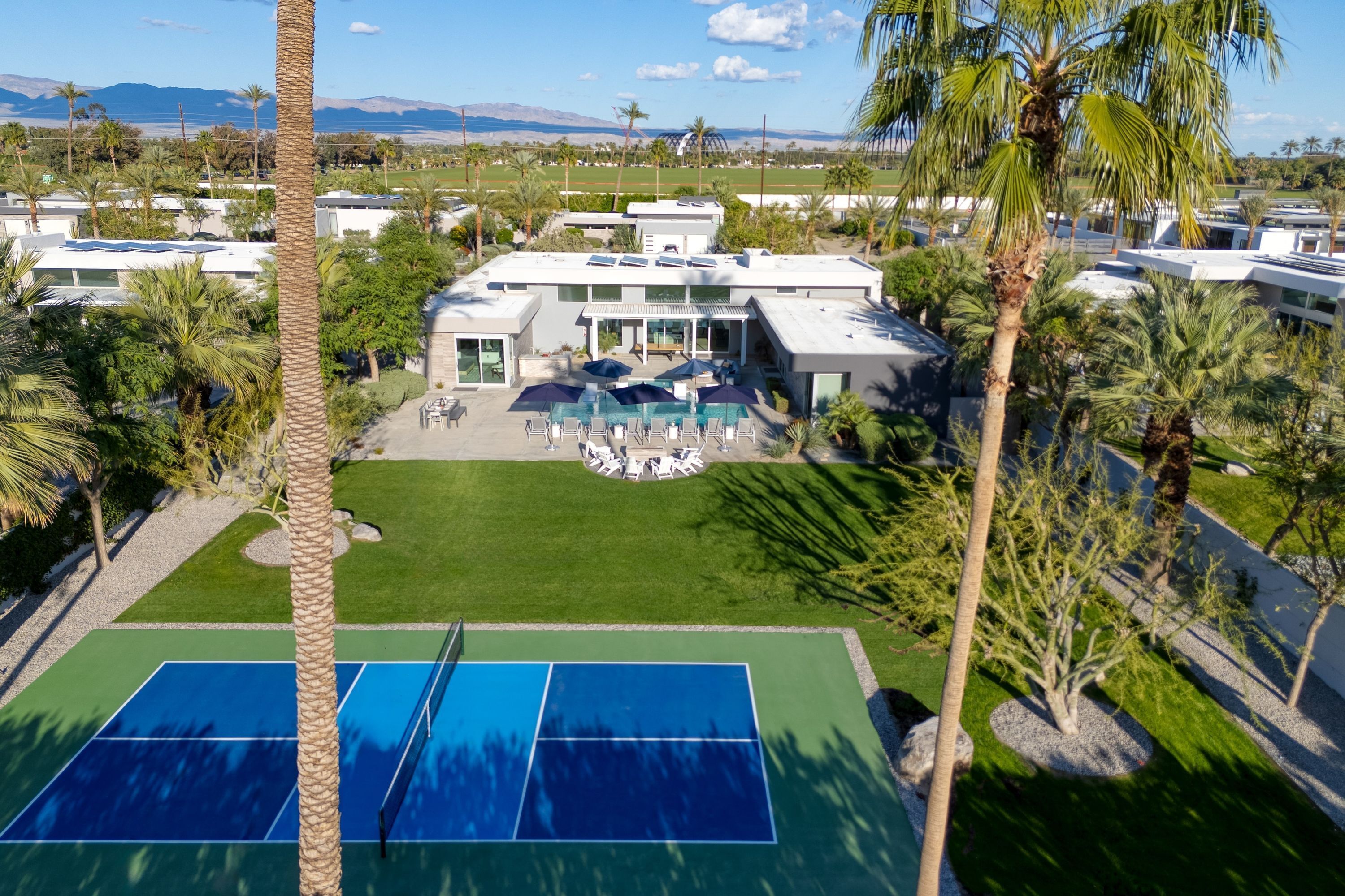 Un resort con cancha de tenis, zona de piscina y una casa grande con patio.