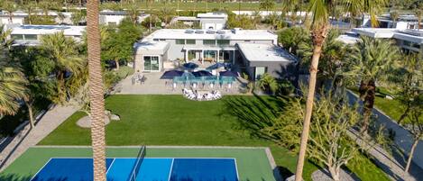 Un resort con cancha de tenis, zona de piscina y una casa grande con patio.