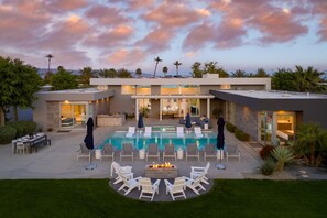 A modern pool area with lounge chairs and a fire pit, surrounded by a landscaped garden and a two-story building with glass doors. - Polo Villa 2 by Avantstay Entertainer s Backyard w Pickleball Court Pool Spa 260314 6 Bedrooms (La Quinta)