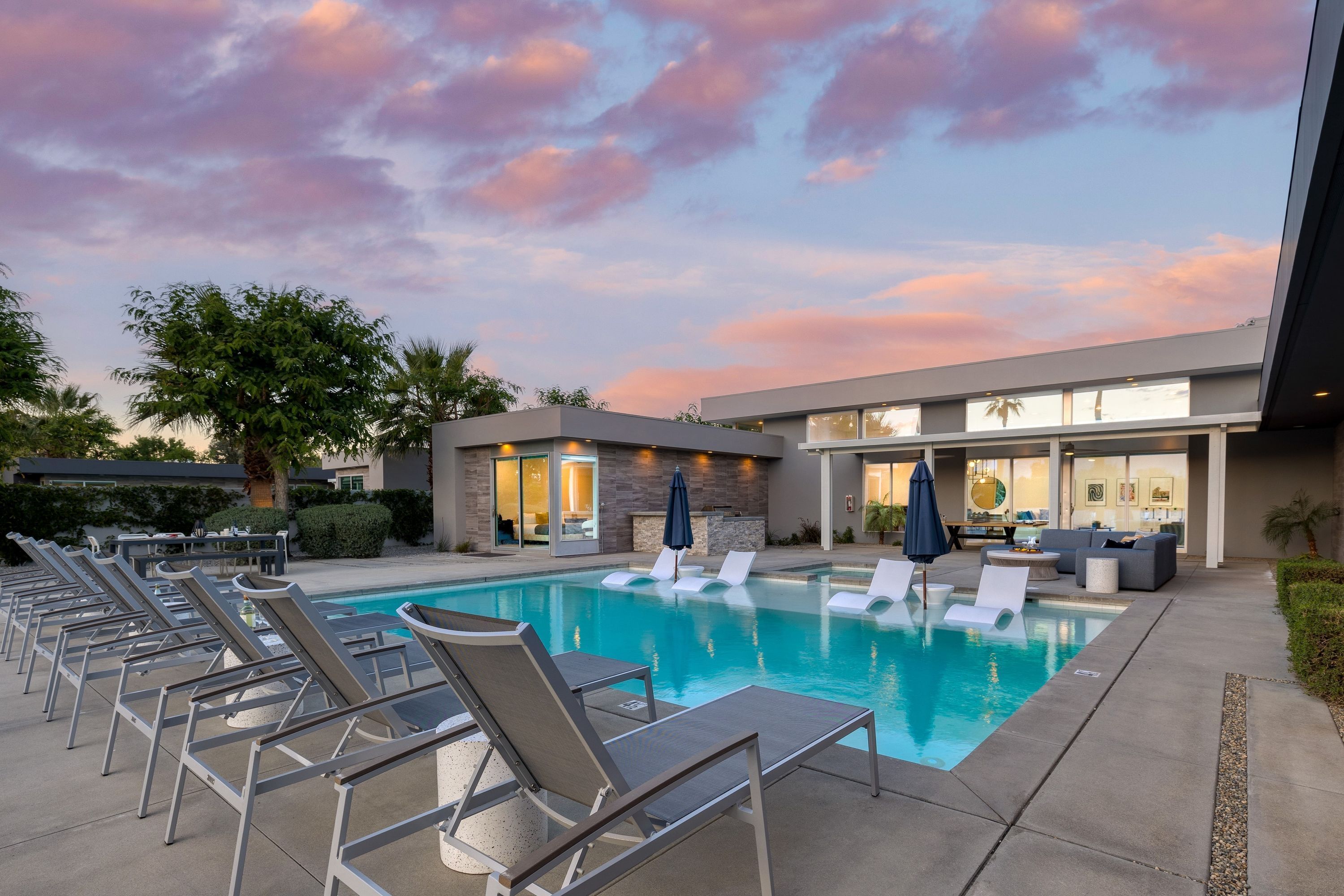 A pool area with lounge chairs and umbrellas, a modern building with large windows, and a clear sky.